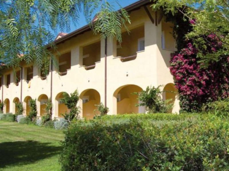 Edificio giallo tra fiori colorati e alberi, atmosfera serena e accogliente.